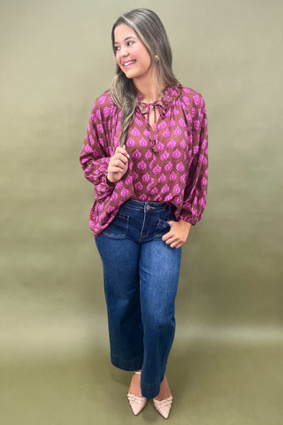 Woman wearing a pink patterned blouse and blue jeans against a green background