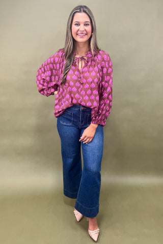 Woman wearing a pink patterned blouse and blue jeans against a beige background
