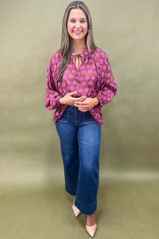 Woman wearing a patterned blouse and jeans on a green background