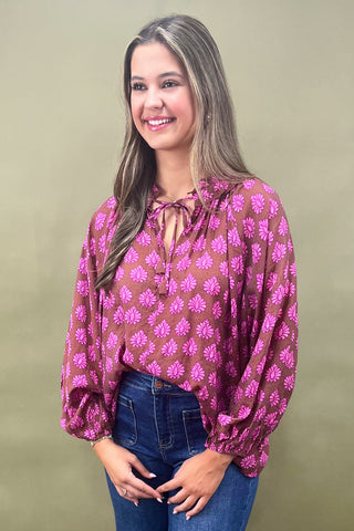 Woman wearing a patterned blouse with long sleeves against a plain background