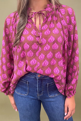 Person wearing a brown blouse with pink floral pattern and blue jeans on a green background