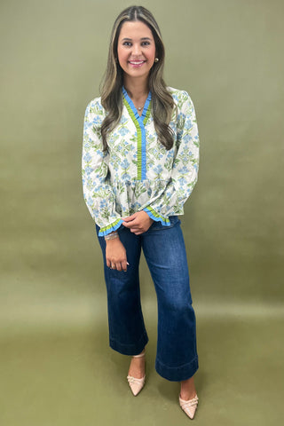 Woman wearing a floral blouse and blue jeans against a green background