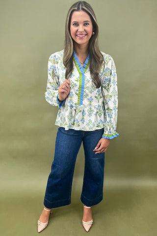 Woman wearing a floral blouse and blue jeans against a green background