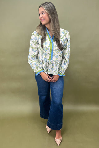 Woman wearing a floral blouse and blue jeans against a beige background