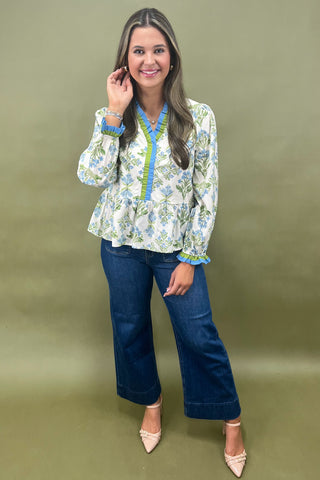 Woman wearing a floral blouse and blue jeans against a green background