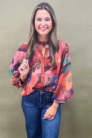 Woman wearing a colorful patterned blouse and blue jeans against a plain background