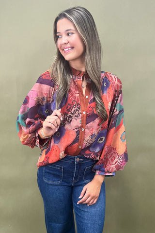 Woman wearing a colorful patterned blouse and blue jeans against a green background