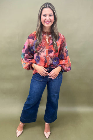 Woman wearing a colorful blouse and blue jeans against a green background