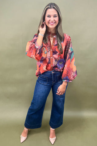 Woman wearing a colorful blouse and blue jeans against a green background