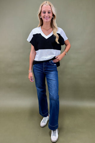 Woman wearing a black and white top with blue jeans on a beige background