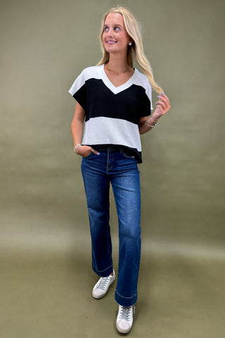 Woman wearing a black and white top with blue jeans on a plain background