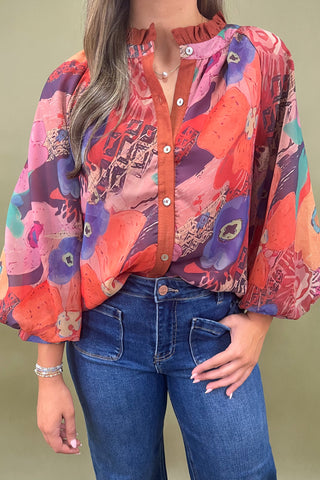 Person wearing a colorful patterned blouse and blue jeans against a green background