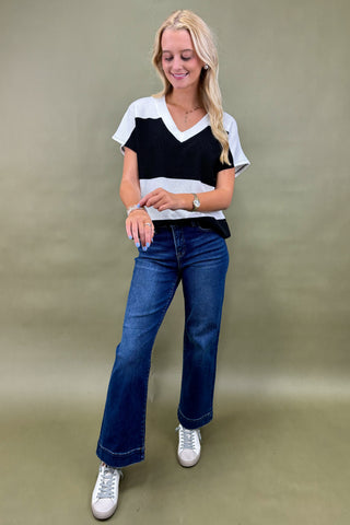 Woman wearing a black and white top with blue jeans on a beige background