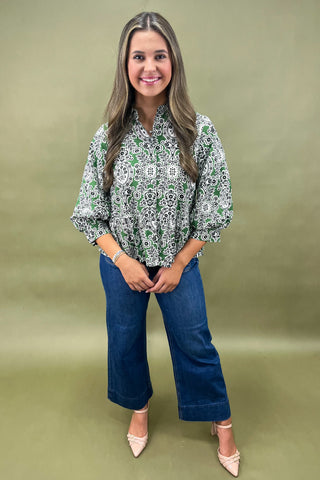 Woman wearing a green patterned blouse and blue jeans against a green background