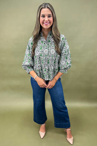 Woman wearing a patterned blouse and blue jeans against a green background