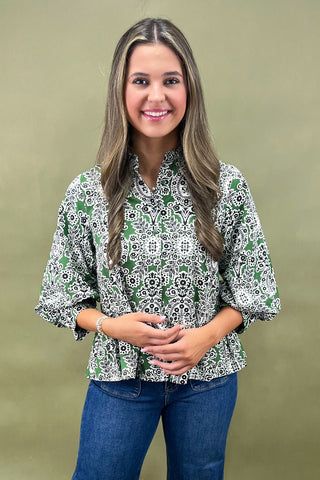 Woman wearing a patterned blouse and jeans against a green background