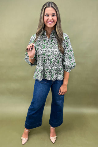 Woman wearing a patterned blouse and blue jeans against a green background