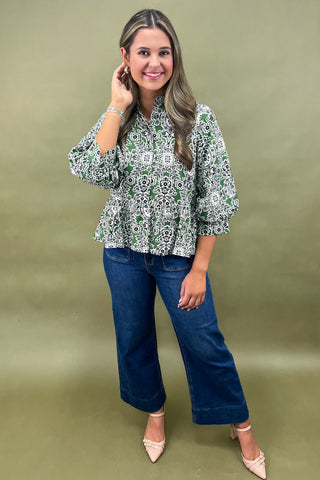 Woman wearing a green and white patterned blouse and blue jeans on a green background