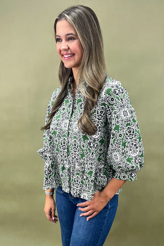 Woman wearing a patterned blouse and blue jeans against a beige background