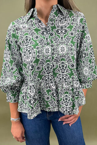 Person wearing a green and white patterned blouse with blue jeans on a beige background