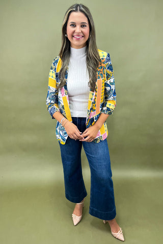 Woman wearing a colorful patterned blazer over a white top and blue jeans on a green background