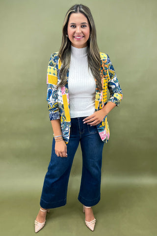 Woman wearing a colorful jacket, white shirt, and blue jeans on a green background