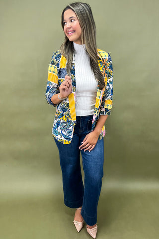 Woman wearing a colorful patterned jacket over a white top and blue jeans on a green background