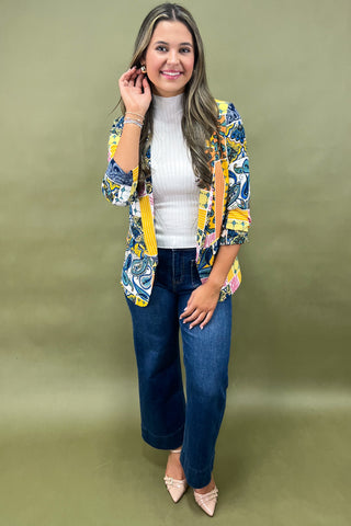 Woman wearing a colorful blazer over a white shirt and blue jeans on a green background