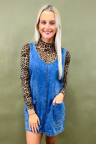 Woman wearing a leopard print top and denim dress against a green background