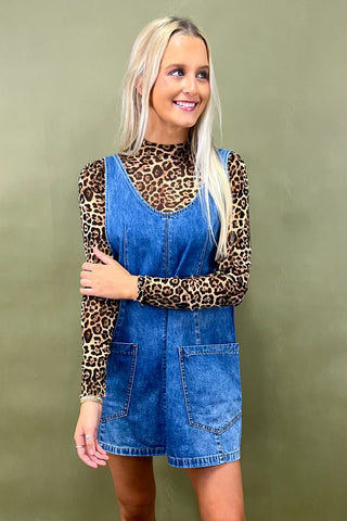 Woman wearing a denim dress over a leopard print top against a green background