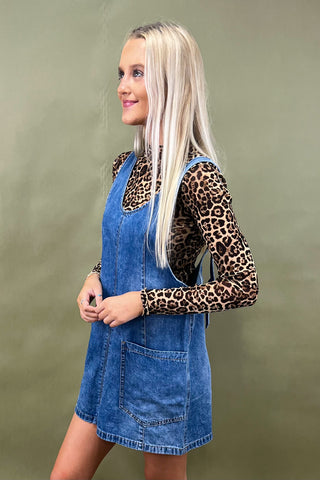 Woman wearing a leopard print top and denim dress against a green background