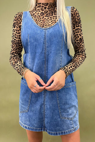 Person wearing a denim dress with leopard print sleeves against a green background