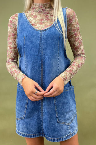 Person wearing a blue denim dress over a floral top against a green background