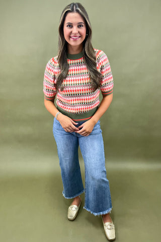 Woman wearing a patterned shirt and jeans against a green background