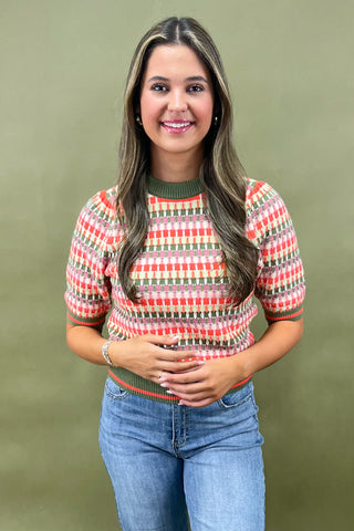 Woman wearing a patterned sweater and jeans against a green background