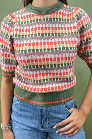 Person wearing a colorful patterned sweater with green trim and blue jeans against a green background