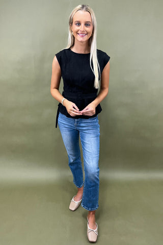 Woman wearing a black top and blue jeans against a green background