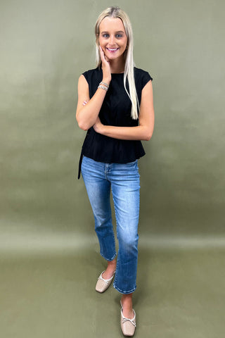 Woman wearing a black sleeveless top and blue jeans against a green background