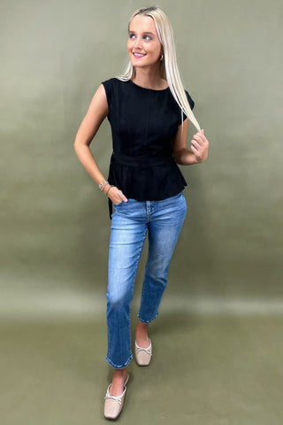 Woman wearing a black sleeveless top and blue jeans against a green background