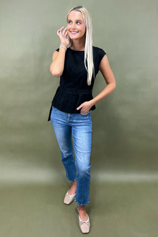 Woman wearing a black sleeveless top and blue jeans against a green background