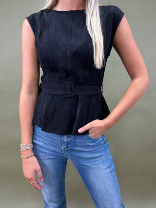 Person wearing a black sleeveless top with a belt and blue jeans on a plain background