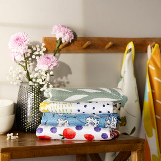 Stack of folded fabric swatches on a wooden table with flowers and a vase in the background.
