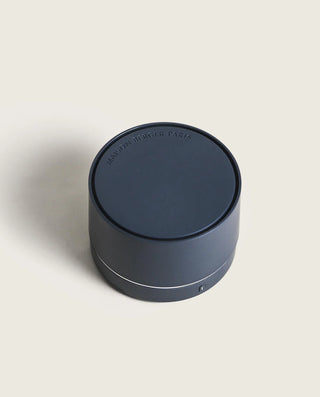 Dark blue cylindrical container with a brand logo on a light beige background