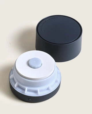 Round white device with a black base on a light beige background