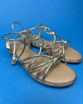 A pair of gold metallic strappy sandals with a tan footbed, against a solid blue background.