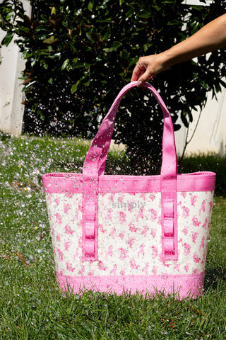 Pink tote bag with floral pattern held by a person outdoors on grass