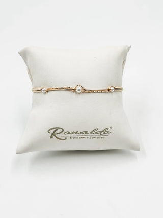 Gold bracelet with a pearl on a white pillow with 'Ronaldo Designer Jewels' branding.