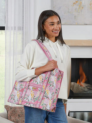 Woman holding a floral quilt in a living room with a fireplace.