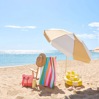 Beach scene with a colorful striped towel, beach chair, umbrella, and pool float on a sandy beach.