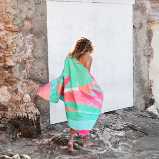 Person wrapped in a colorful towel standing in front of a white wall.